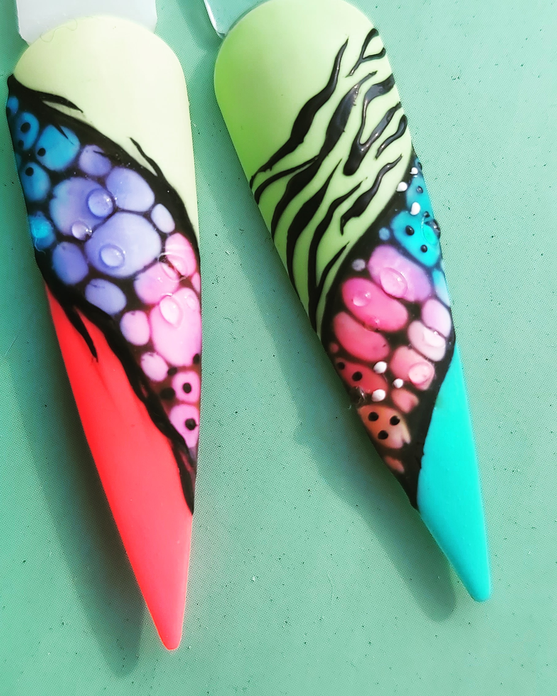 Twee stiletto-nagels met cellen en zebrastrepen op een mintgroene achtergrond