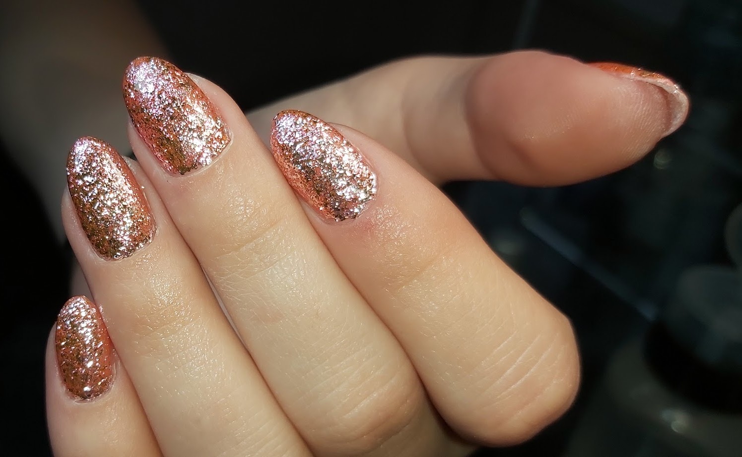 Amandelnagels vol rosé glitter tegen een zwarte achtergrond